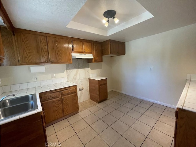 kitchen featuring light tile patterned flooring, sink, tile counters, and a tray ceiling