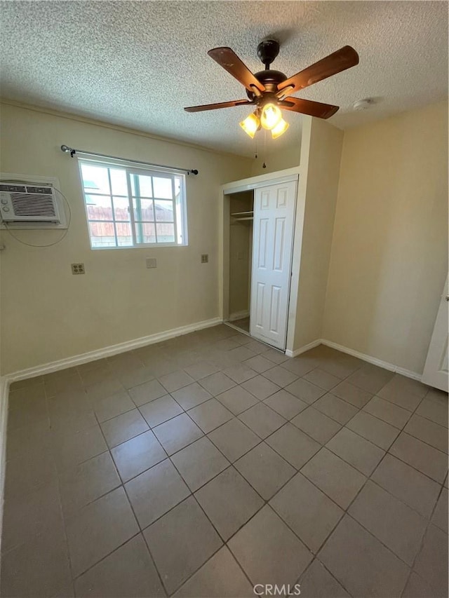 unfurnished bedroom featuring ceiling fan, light tile patterned floors, a textured ceiling, an AC wall unit, and a closet