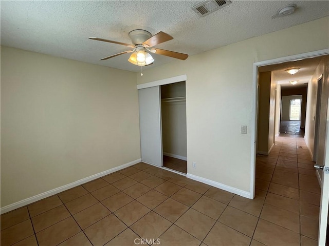 unfurnished bedroom with a textured ceiling, a closet, light tile patterned floors, and ceiling fan