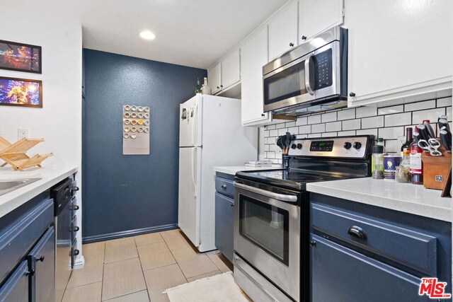 kitchen featuring appliances with stainless steel finishes, blue cabinets, white cabinetry, and backsplash