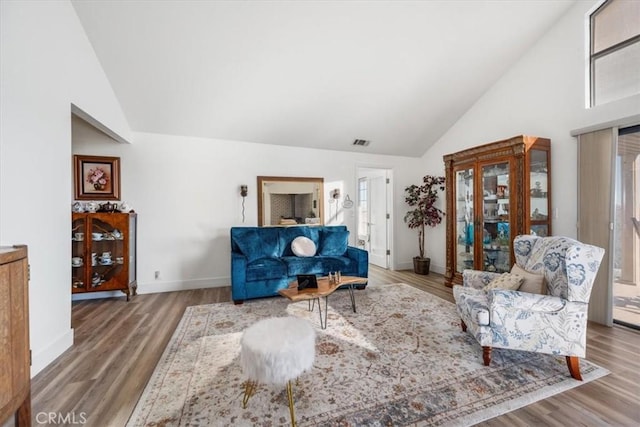 living area with wood finished floors, high vaulted ceiling, baseboards, and visible vents