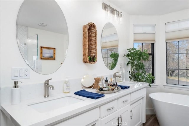 bathroom with double vanity, visible vents, a sink, and a freestanding tub