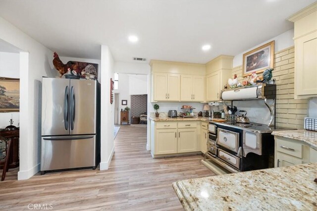 kitchen with light stone counters, cream cabinets, light hardwood / wood-style floors, and appliances with stainless steel finishes