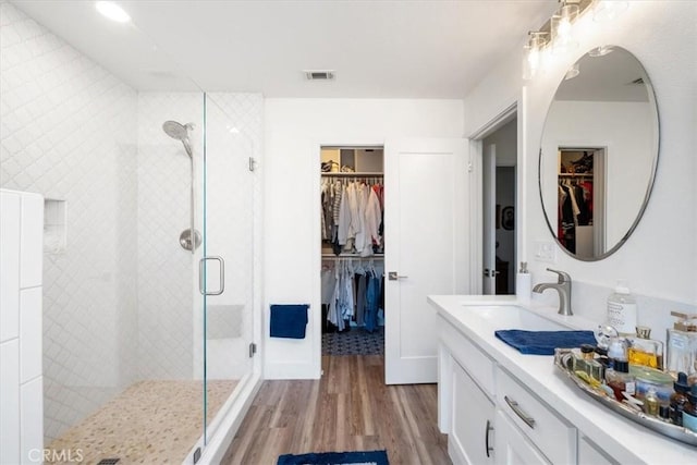 full bathroom featuring visible vents, a shower stall, wood finished floors, vanity, and a walk in closet
