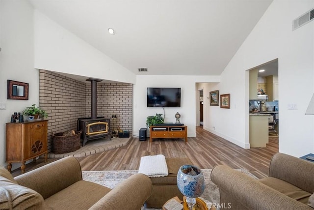 living room with wood-type flooring, high vaulted ceiling, and a wood stove