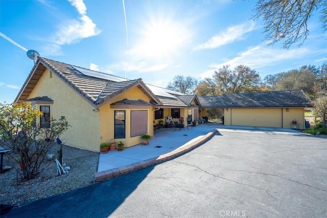 exterior space featuring a tile roof, stucco siding, an attached garage, aphalt driveway, and solar panels
