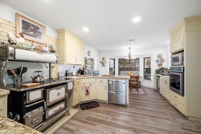 kitchen featuring light wood-style flooring, visible vents, a peninsula, stainless steel appliances, and a notable chandelier