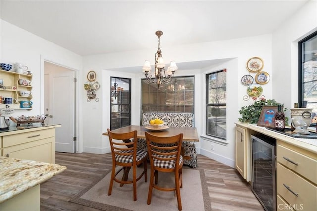 dining space with a healthy amount of sunlight, wine cooler, an inviting chandelier, and light wood finished floors
