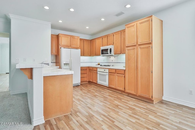 kitchen featuring kitchen peninsula, white appliances, light hardwood / wood-style flooring, ornamental molding, and tile counters