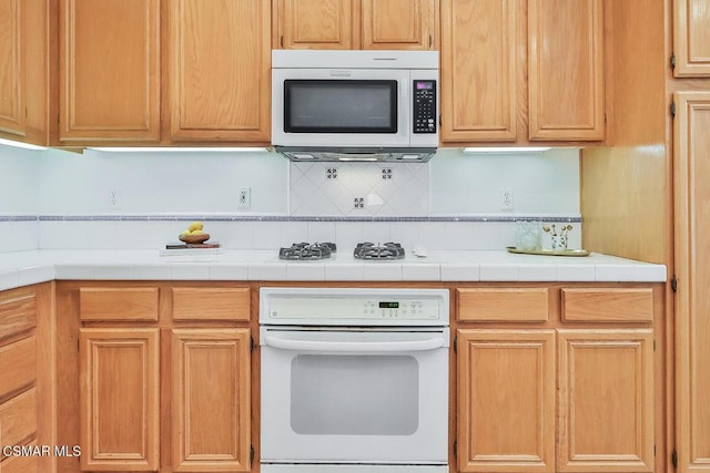 kitchen with tile countertops, decorative backsplash, and white appliances