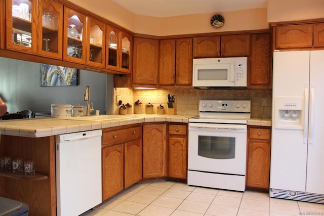 kitchen featuring sink, tasteful backsplash, tile countertops, white appliances, and light tile patterned floors