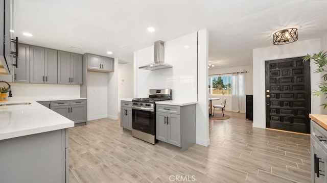 kitchen with sink, wall chimney exhaust hood, stainless steel range with gas stovetop, and gray cabinetry