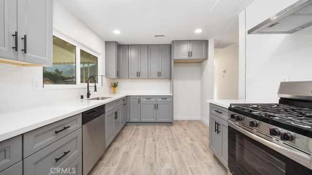 kitchen featuring appliances with stainless steel finishes, sink, light wood-type flooring, gray cabinetry, and range hood