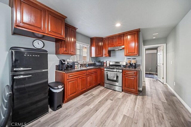 kitchen featuring sink, stainless steel range with gas cooktop, light wood-type flooring, black refrigerator, and dark stone counters