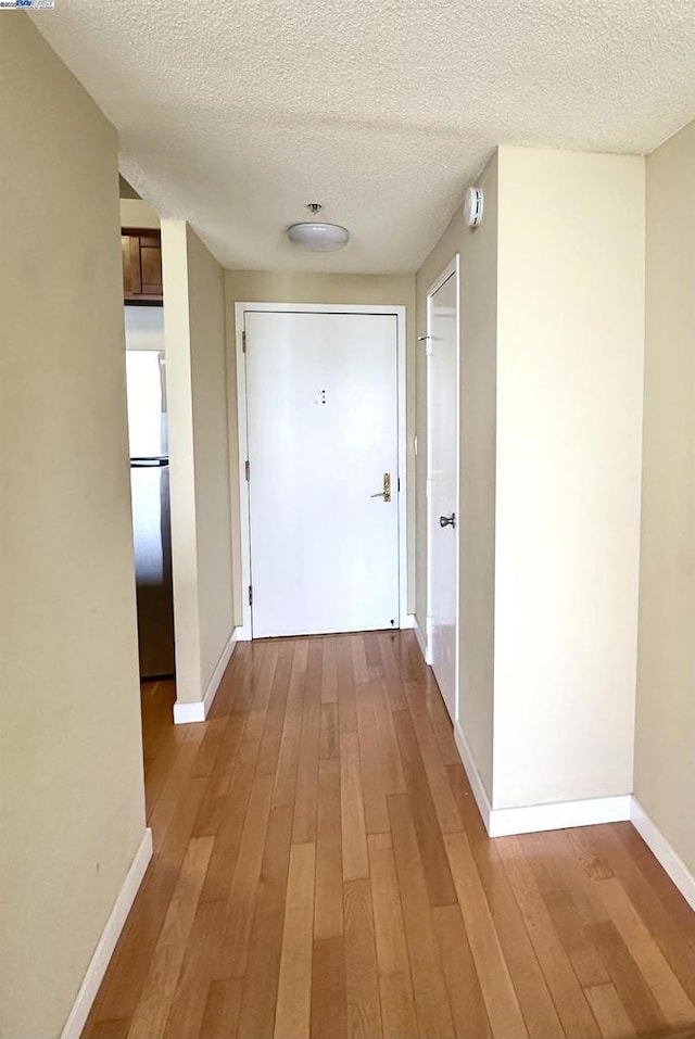 corridor with a textured ceiling and light hardwood / wood-style flooring