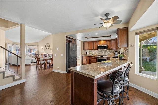 kitchen with ceiling fan, kitchen peninsula, a tray ceiling, light stone countertops, and stainless steel appliances