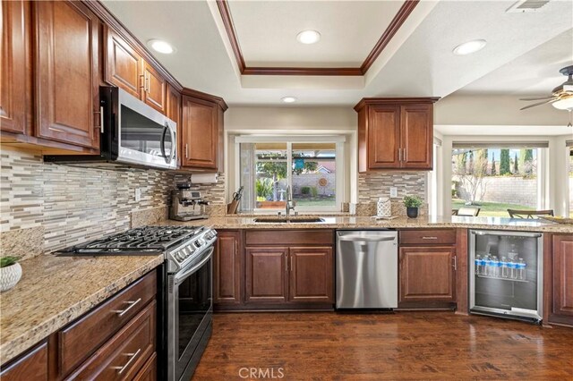 kitchen with a raised ceiling, sink, crown molding, stainless steel appliances, and beverage cooler