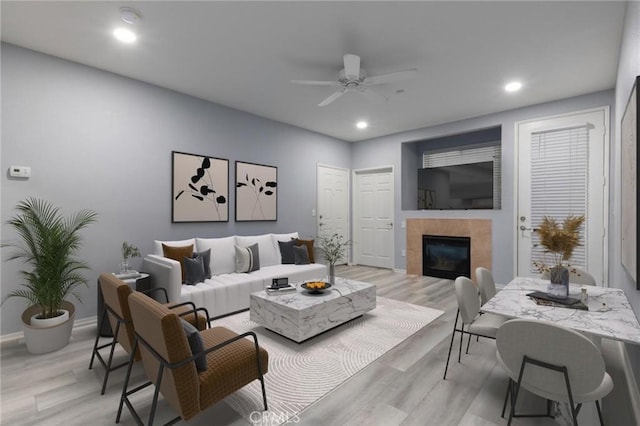 living room with ceiling fan, a tile fireplace, and light hardwood / wood-style flooring