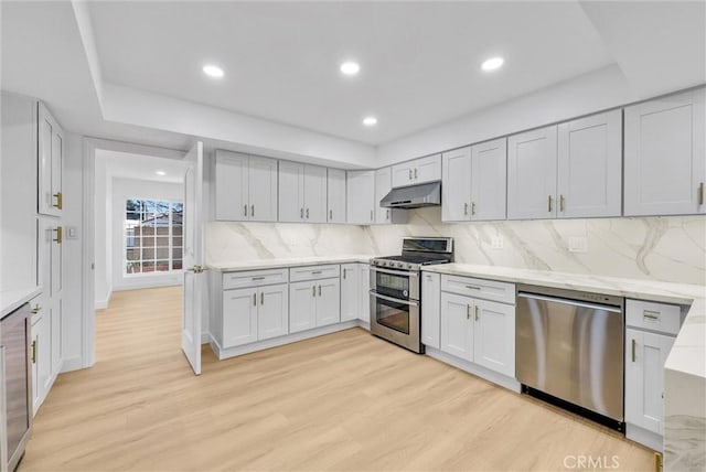 kitchen featuring light stone countertops, tasteful backsplash, light hardwood / wood-style floors, and appliances with stainless steel finishes