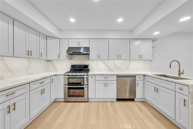 kitchen with stainless steel appliances, sink, white cabinetry, light hardwood / wood-style floors, and tasteful backsplash