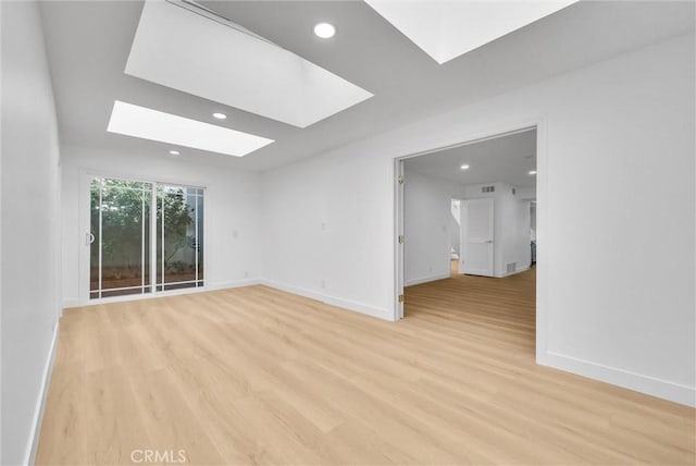 unfurnished room featuring a skylight and light hardwood / wood-style flooring