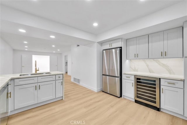 kitchen with stainless steel fridge, tasteful backsplash, light wood-type flooring, beverage cooler, and sink