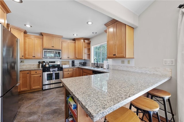 kitchen featuring kitchen peninsula, a breakfast bar area, appliances with stainless steel finishes, light stone counters, and sink