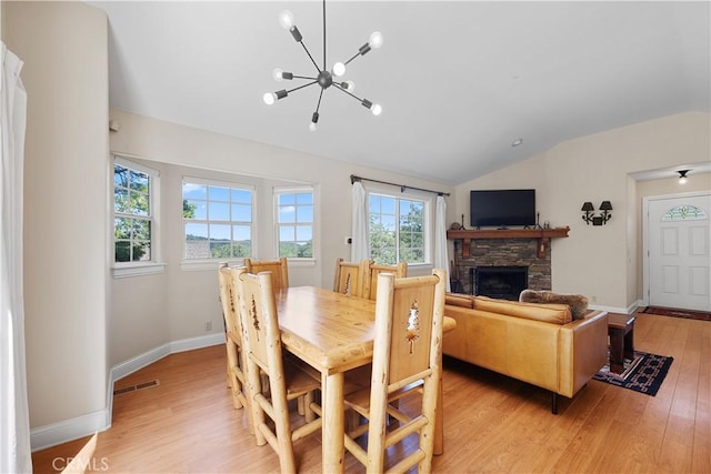 dining area with lofted ceiling, light wood-type flooring, a stone fireplace, and a chandelier