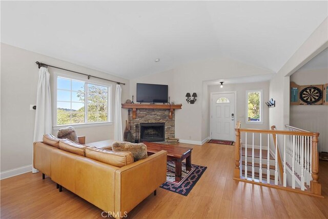 living room featuring lofted ceiling, a stone fireplace, and light hardwood / wood-style floors