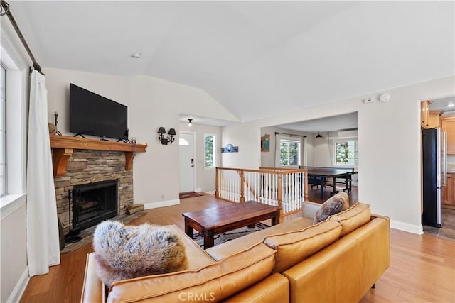 living room with light wood-type flooring, vaulted ceiling, a fireplace, and plenty of natural light