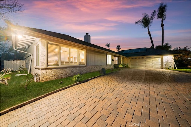 single story home with a garage, a lawn, and solar panels