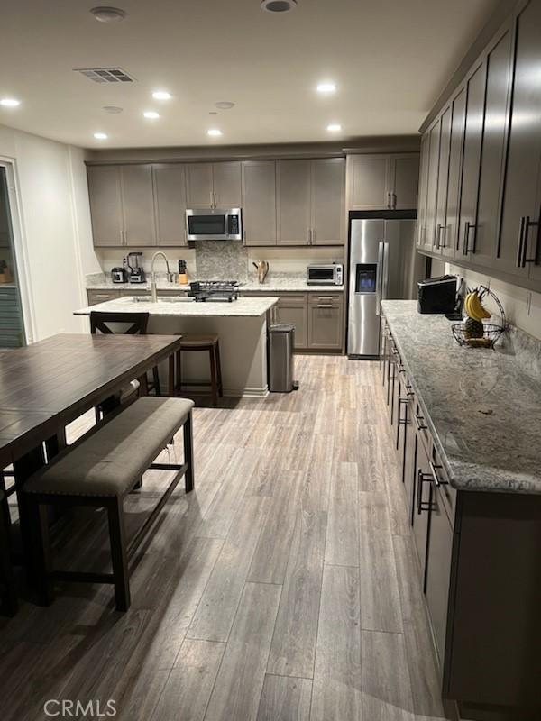 kitchen with stainless steel appliances, dark stone counters, an island with sink, sink, and light hardwood / wood-style flooring