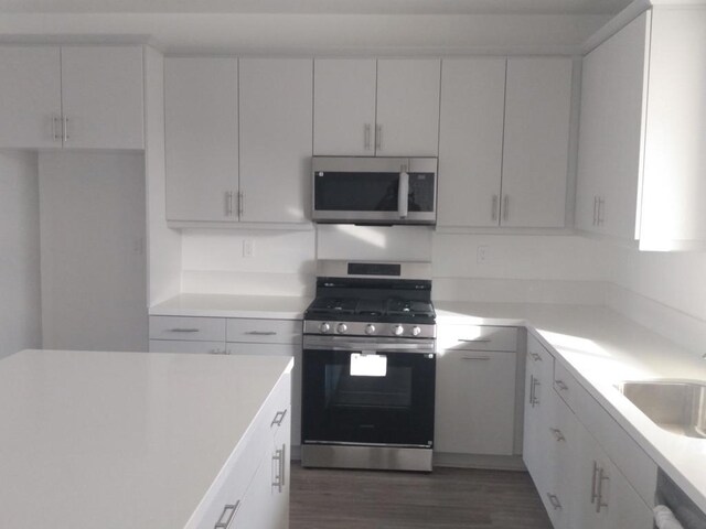 kitchen with dark wood-type flooring, stainless steel appliances, white cabinets, and sink