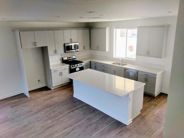 kitchen with appliances with stainless steel finishes, a center island, sink, hardwood / wood-style flooring, and gray cabinetry