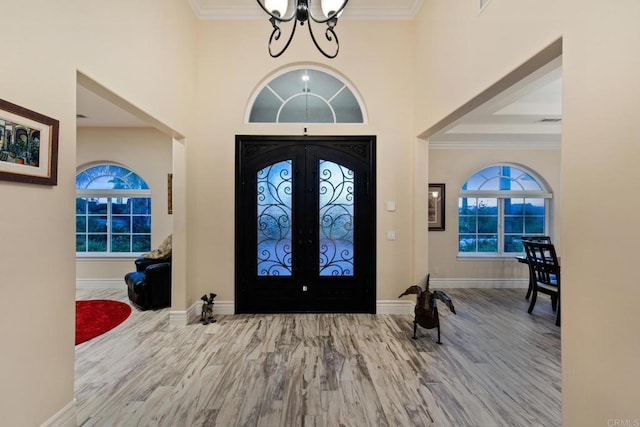 entryway with wood finished floors, baseboards, ornamental molding, french doors, and an inviting chandelier