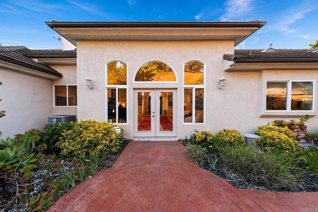 entrance to property with stucco siding, central AC unit, and french doors