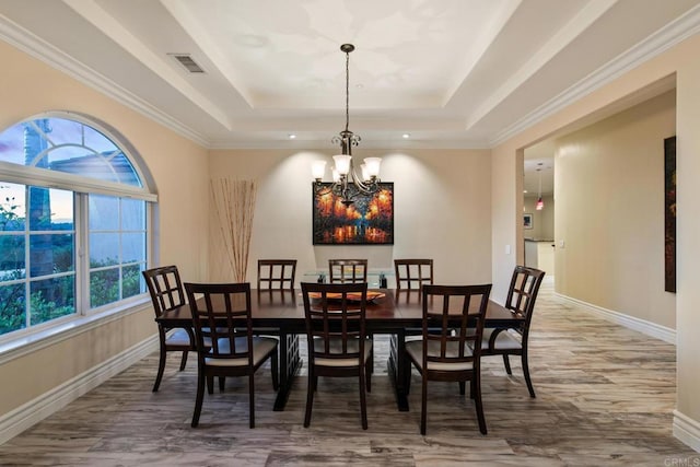 dining room with baseboards, visible vents, a tray ceiling, and wood finished floors