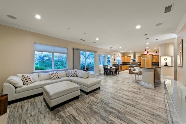 living area featuring a wealth of natural light, ornamental molding, visible vents, and recessed lighting