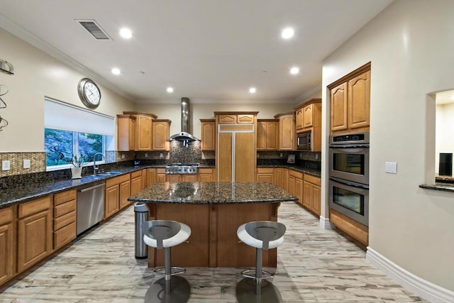 kitchen featuring visible vents, wall chimney exhaust hood, a kitchen island, built in appliances, and a sink