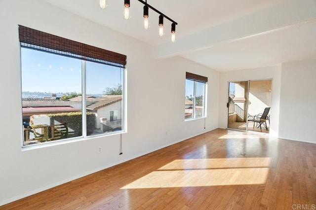 unfurnished room with beamed ceiling, wood-type flooring, a healthy amount of sunlight, and track lighting