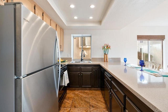 kitchen with sink, stainless steel fridge, black gas range, dark brown cabinets, and a tray ceiling