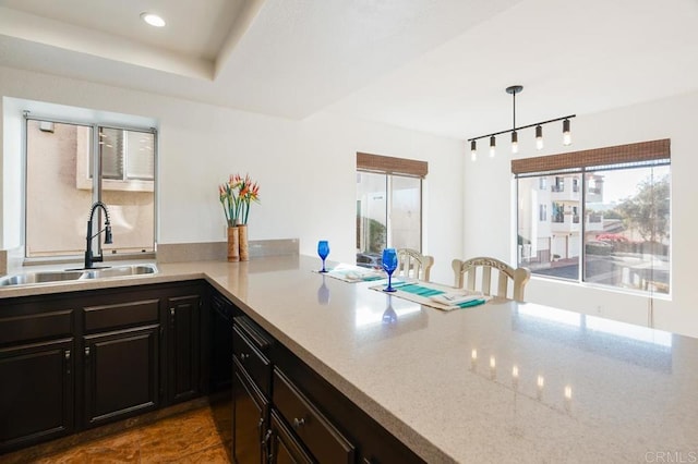 kitchen with hanging light fixtures, light stone countertops, sink, and kitchen peninsula