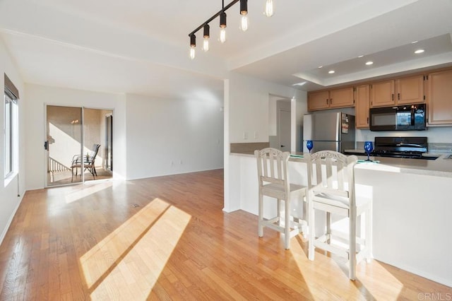 kitchen with a raised ceiling, range, stainless steel refrigerator, and light hardwood / wood-style flooring