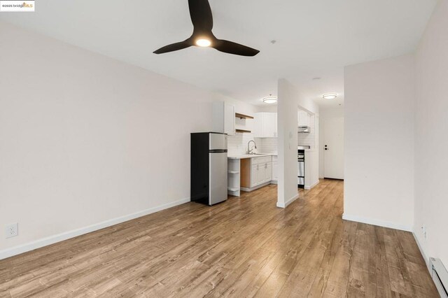 unfurnished living room featuring ceiling fan, baseboard heating, sink, and light hardwood / wood-style flooring