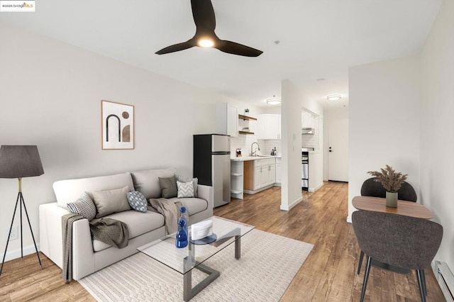 living room featuring ceiling fan, sink, a baseboard heating unit, and light hardwood / wood-style floors