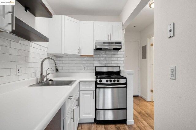 kitchen with light hardwood / wood-style floors, stainless steel range, backsplash, white cabinets, and sink