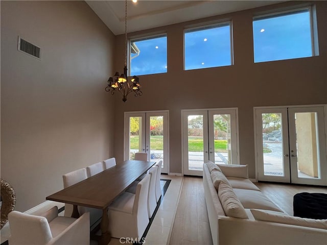 dining space featuring high vaulted ceiling, light hardwood / wood-style floors, a notable chandelier, and french doors