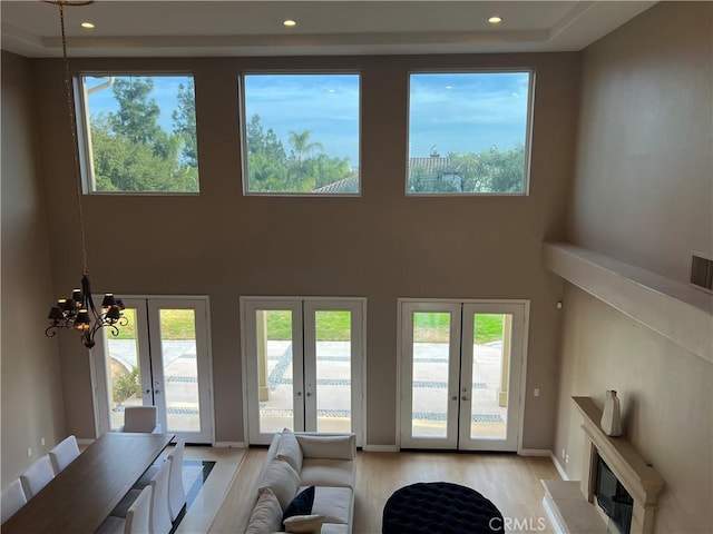 living room featuring french doors, a towering ceiling, a chandelier, and light hardwood / wood-style flooring