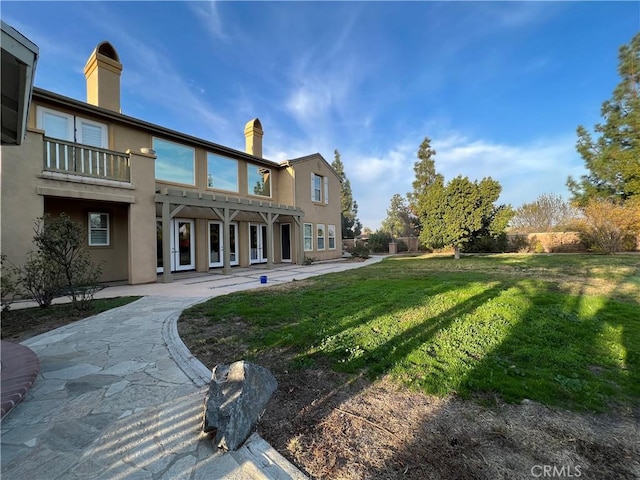 rear view of property featuring a balcony and a lawn