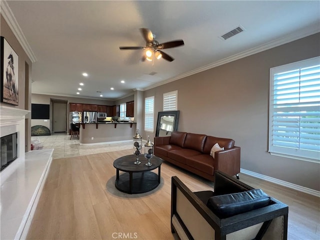 living room featuring light hardwood / wood-style floors, crown molding, ceiling fan, and a fireplace